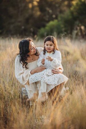 A child cuddled close to their mum as the sun dips behind the trees, a heartwarming outdoor family photography moment