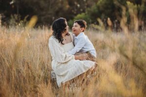 A boy sits in his mum's lap cuddling in long grass, a tender and natural family photography moment in Ingleburn