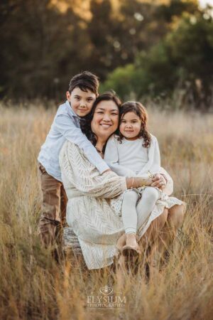 Family sitting together in a winter field at sunset, wrapped in warm light during an outdoor session with a South West Sydney family photographer