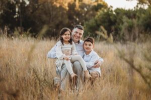 Family sitting together in a winter field at sunset, wrapped in warm light during an outdoor session with an Ingleburn family photographer
