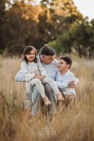 Family sitting closely together in soft golden light, captured by a family photographer during a relaxed sunset outdoor session