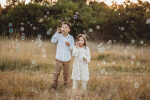Kids blowing bubbles standing in tall grass at sunset, a playful and fun‑filled moment from their outdoor family photography session