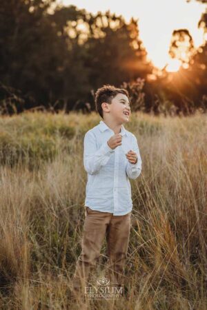 Kid standing in tall grass with the golden sunset behind, captured during a joyful Ingleburn family session