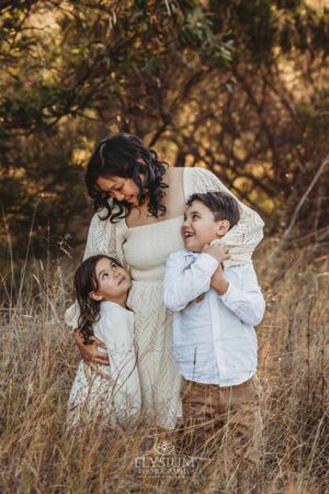 A mother hugs her children in warm golden light, a natural and heartfelt moment from their outdoor family photography session