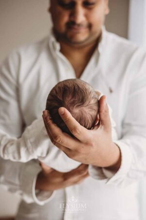 Close view of a newborn baby's head held gently by her father's hands during a studio session in Ingleburn