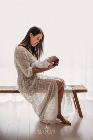 Mother sitting on a wood bench holding her newborn in an Ingleburn natural light studio