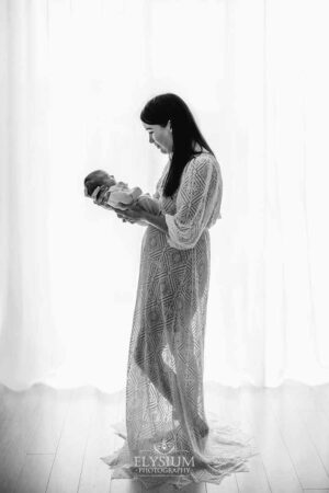 Mother holding her newborn in front of a large window with gentle natural light in an Ingleburn studio